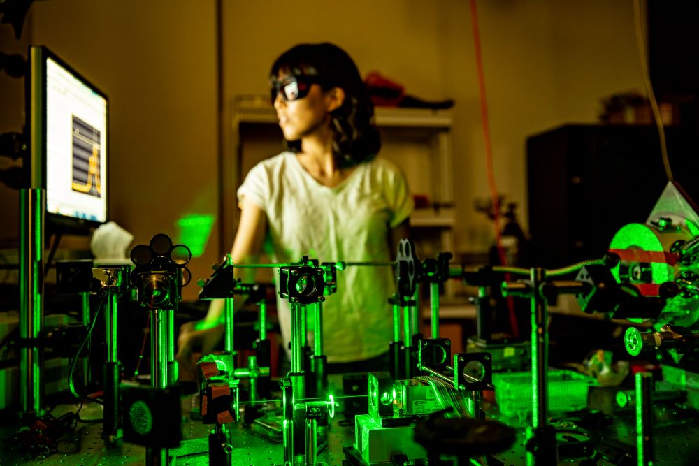 A woman stands behind lab equipment that is generating a series of green lasers