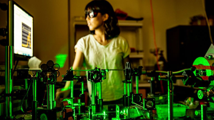 A person stands behind lab equipment that is generating a series of green lasers