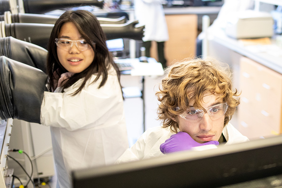 Students in white lab coats and goggles conducting an experiment.