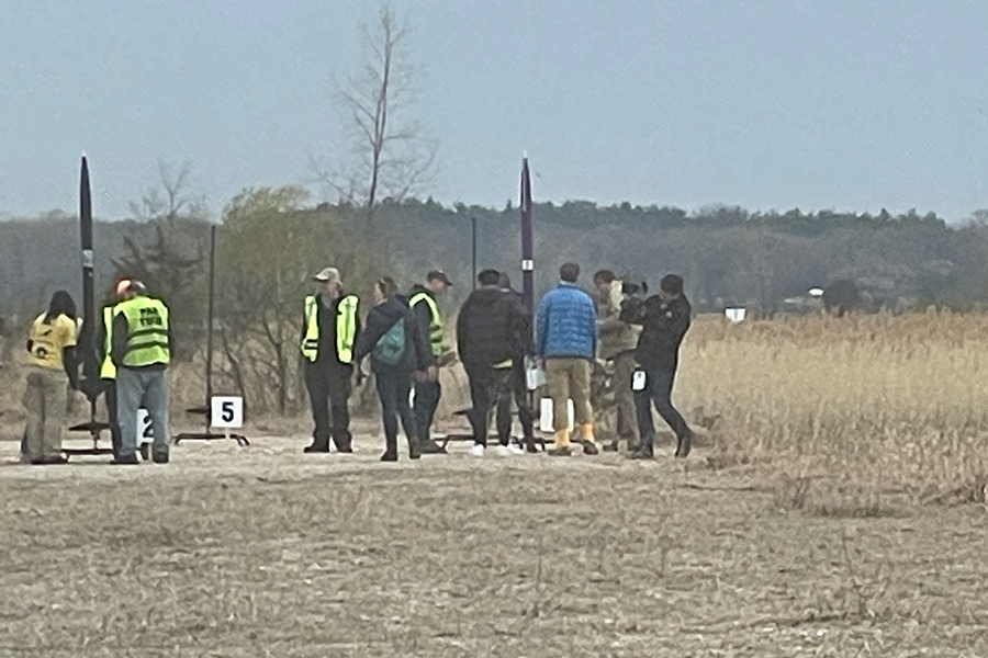 The UW FNL team from a distance, standing their rocket upright in a large field, preparing for competition launch.