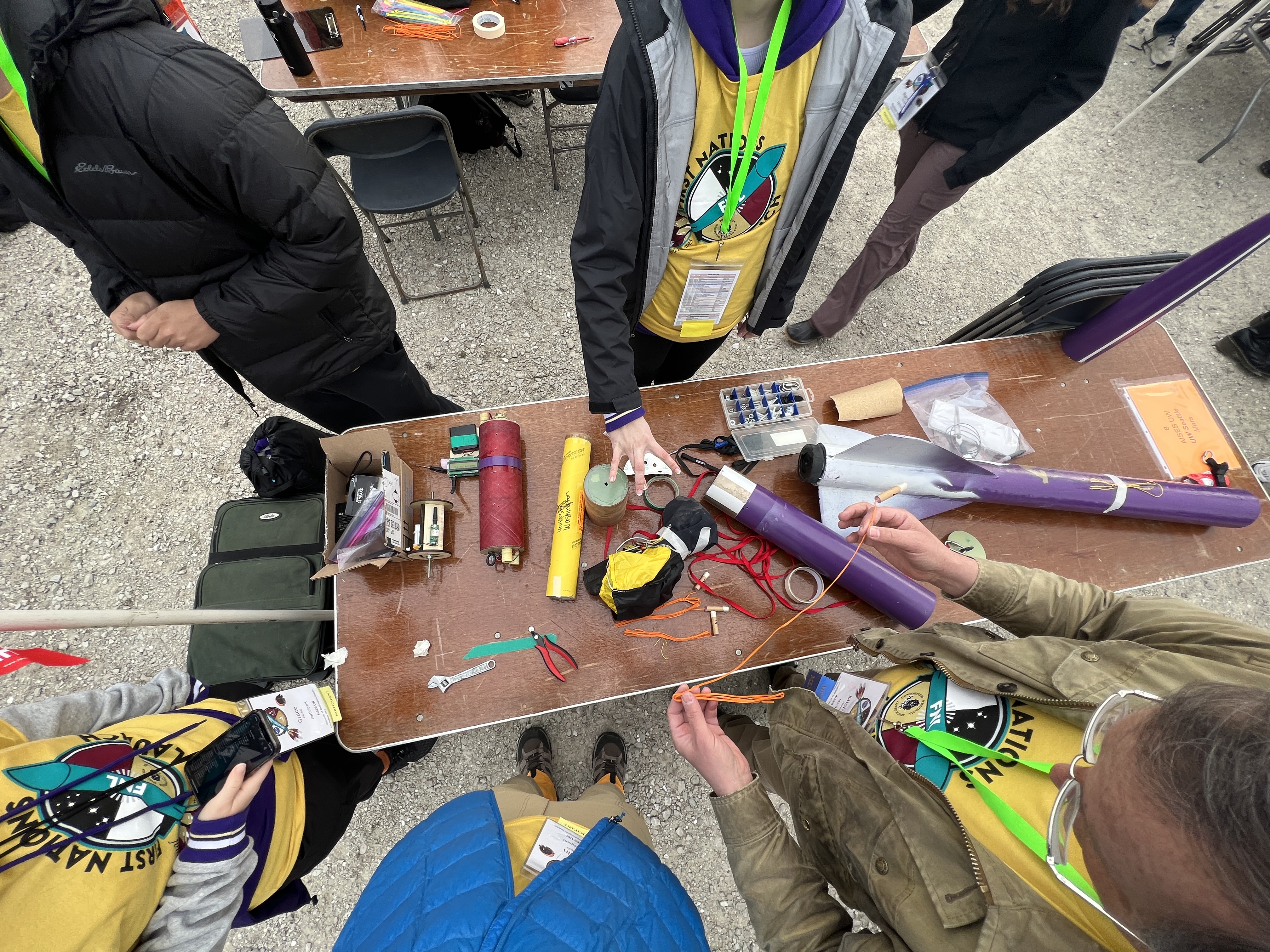 The pieces of a disassembled rocket on a table, viewed from above, surrounded by the members of the UW FNL team.