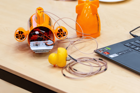 A small orange model of a submarine on a table. The submarine has wiring inside of it.