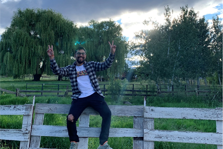 Alan Ricardo Medina sitting on a fence, giving peace signs with his hands, as the sun sets behind him.