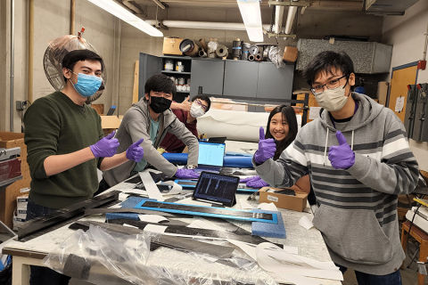 A group of five students around a work table covered in scraps of materials.