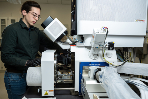 Jack Grimm, UW doctoral student in materials science and engineering, stands behind a large white scanning electron microscope and prepares an enamel sample.